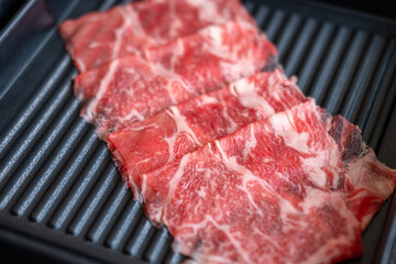 A close-up shot of sliced raw meat, arranged on a plate, ready to be cooked in a hot pot