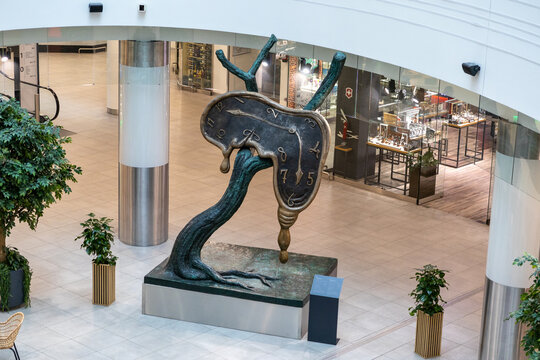 Wroclaw, Poland - January 25, 2025: melting clock sculpture on tree branch in shopping mall with modern decor and glass storefronts in the background