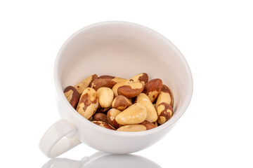 Brazil nuts without shells in a white ceramic cup, macro, isolated on a white background.