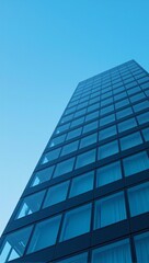 Obraz premium Minimalist skyscraper with reflective dark tinted glass windows against a bright blue sky