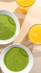 Two bowls of vibrant green soup paired with glasses of orange juice on a wooden table, symbolizing healthy eating