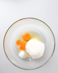 A glass bowl contains sugar and eggs on a white background, representing baking preparation for festive holiday desserts