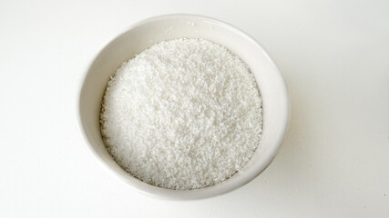 A bowl of shredded coconut on a white surface, ideal for baking, tropical recipes, or holiday desserts