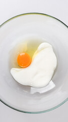 A glass bowl contains an egg and cream, symbolizing baking preparation for Easter or holiday desserts
