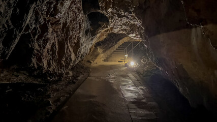 Dimly lit cave tunnel with stone stairs and rugged walls, ideal for exploring adventure tourism or geological formations