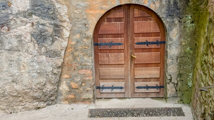 An arched wooden door set in a rustic stone wall evokes medieval architecture, symbolizing mystery...