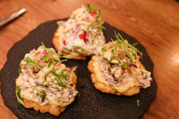 close up of Peruvian traditional cold cut appetiser dish of deep fried corn bread, shredded chicken, tartar sauce, yellow chilli sauce