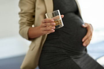 Woman, pregnant and drinking alcohol in office, prenatal danger and depression in workplace. Female person, hands and harm baby in belly with whiskey glass, toxic beverage and parent neglect of fetus