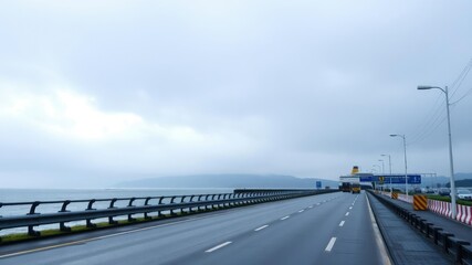 Fototapeta premium Overcast sky with misty rain falling on the road to the ferry terminal, rainy day, scenery, travel