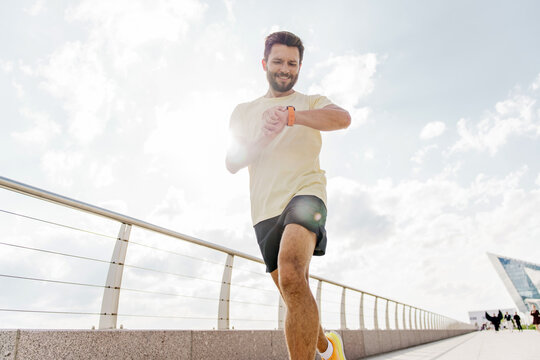 Man jogging on an outdoor pathway while checking his smartwatch in bright sunlight