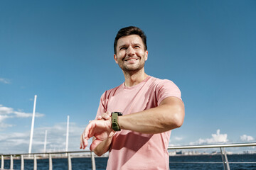 Smiling man checks watch while enjoying a sunny day by the waterfront in a coastal city