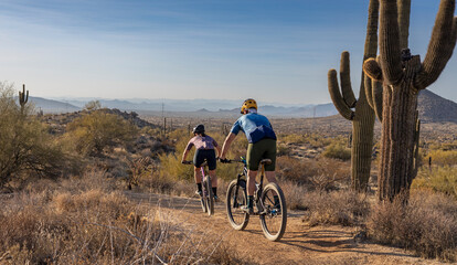 Two Mountain Bikers Riding Down An Elevated Desert Trail In Arizona