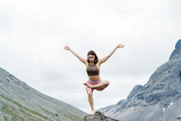 Woman practicing yoga in a mountain landscape during cloudy weather
