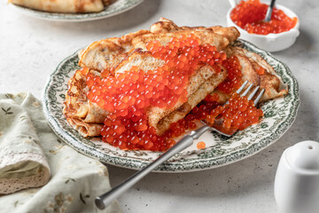 Pancakes or crepes with red caviar on a plate on white texrured background. Blini for Maslenitsa, recipe