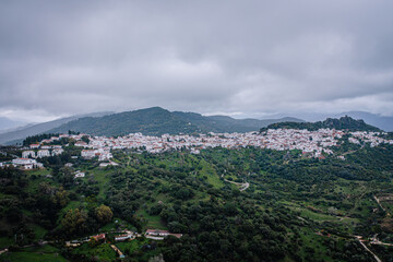 Panoramic view of a picturesque white village nestled in lush green hills under a cloudy sky, showcasing traditional Andalusian architecture.