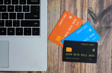 Three credit cards on a wooden table placed next to a laptop