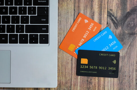 Three credit cards on a wooden table placed next to a laptop - Powered by Adobe