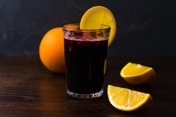 Delicious mulled wine with orange, cinnamon and honey in a glass on a dark background. Concept of a cozy winter evening, Christmas and New Year celebration