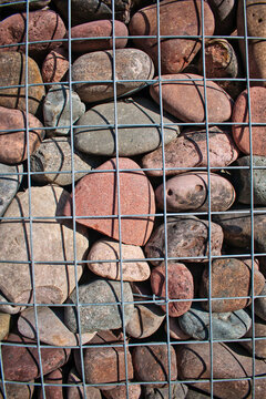 A visually captivating close-up image of a collection of multicolored smooth river rocks enclosed within a metal wire grid. This composition highlights the natural beauty and diversity of the stones.