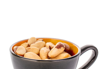 Brazil nuts without shells in a black ceramic cup, macro, isolated on white background.