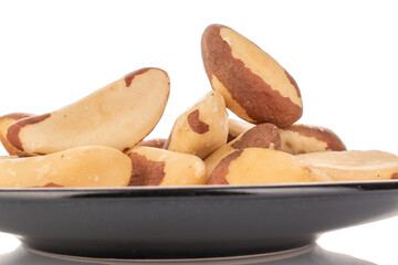 Brazil nuts without shells on a black ceramic saucer, macro, on a white background.
