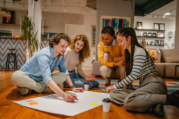 multicultural colleagues gather around a large paper on a wooden floor