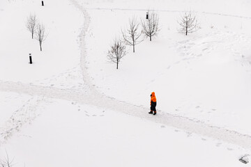 Worker in an orange jacket standing on a snowy path in winter, top-down view