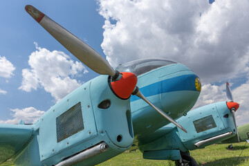Blue propeller airplane standing on a grassy area against blue sky with clouds. Horizontally. 