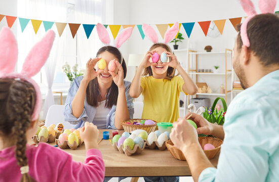 Cheerful family wearing bunny ears decorating colorful Easter eggs together at home. Happy parents and children enjoying festive activity, having fun, laughing and creating joyful holiday memories.