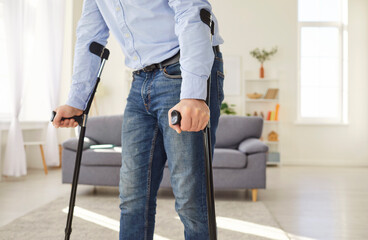 Close up shot of a man walking with crutches at home during rehabilitation after trauma or injury....