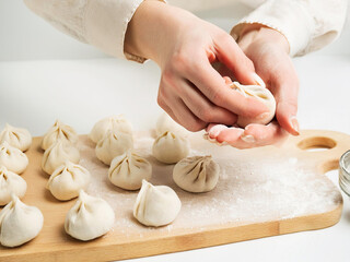 Hands are shown in the process of making dumplings, with several already formed dumplings placed on...