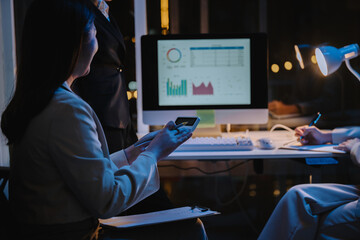 Businesswomen analyzing financial data on a computer and calculator, working late in the office at night