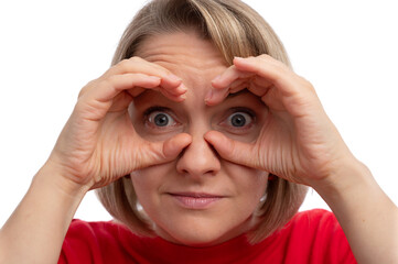 A woman playfully making a funny face with her hands shaped like glasses against a white background.