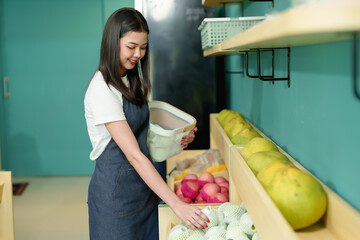 Beautiful Asian small business fruit shop owner. Young woman organizing fresh seasonal fruit in wooden baskets at grocery store. Local organic market with tropical produce.