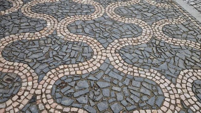 ripples pattern from mosaic cubes on black rough pavement. squares and dashed lines. promenade in the square with repeating lines of the shape of waves and hearts
