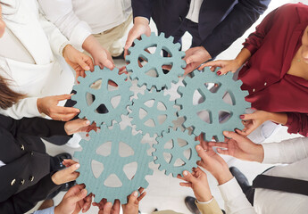 Close-up view of people team hands together holding gears or cogwheels in a circle, symbolizing...