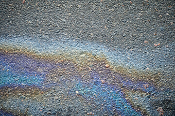 Gasoline or oil spill generates vibrant patterns on the asphalt road, signaling environmental...
