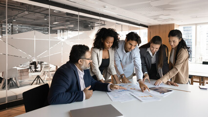 Focused diverse company employees reviewing statistic documents, marketing data in paper documents together, discussing further business strategy, planning task, teamwork