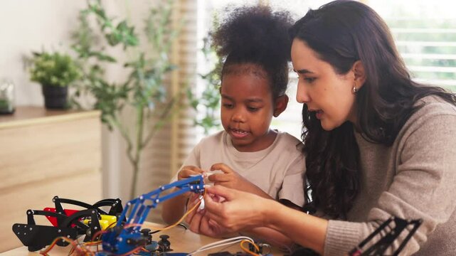 Loving mother guiding her daughter through a robotics project, engaging in a fun hands-on STEM learning activity that fosters problem-solving, creativity, and early engineering skills at home