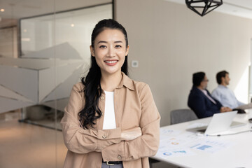 Happy confident young Asian businesswoman posing in meeting room with colleagues in teamwork...