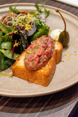 Marinated steak tartar raw beef meat served on bread toasts with green salad in German restaurant