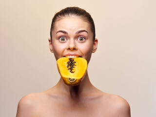 Surprised woman holding a ripe papaya in front of her mouth with wide open eyes and a curious...