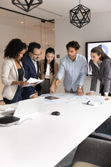 Mature boss and team of young multiethnic employees analyzing marketing reports, discussing...