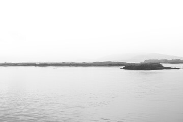Black and white photograph captures a tranquil seascape in Iceland, featuring calm waters,...