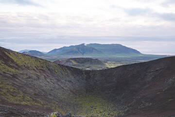 Volcanic landscapes of the Snaefellsnes Peninsula in Iceland, with vast craters, rugged terrain, and distant green mountains under a cloudy sky