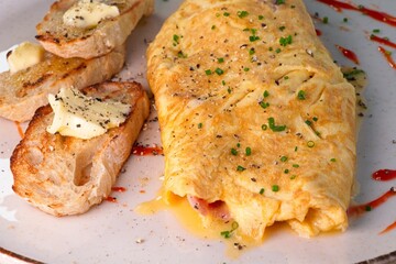 The omelette is plated on a charming dish alongside grilled sourdough bread, butter, and chives, showcased against a rustic tablecloth with pumpkin embellishments.