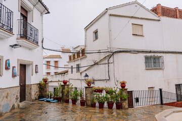 Courtyard in Gaucín, Spain, with potted plants, stone pavement, wrought iron railings, whitewashed buildings, and a cloudy sky creating a serene atmosphere.