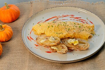 Omelette is served on a rustic plate with grilled sourdough bread, butter, and chives, all presented on a rustic tablecloth with pumpkin decorations.
