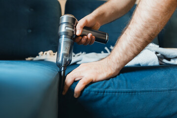 Male adult using handheld vacuum to clean blue sofa