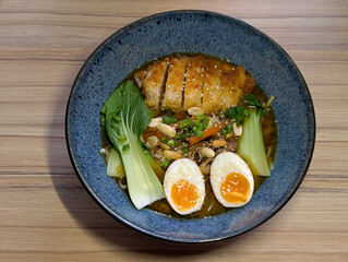 a blue ceramic bowl of delicious miso ramen soup with pak choi, egg, fried chicken, sesame seeds, peanuts and spring onions